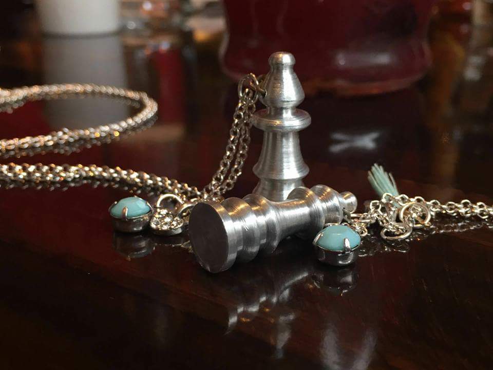 two metal turned chess pieces attahced to a chain and some charms to make them pendants.